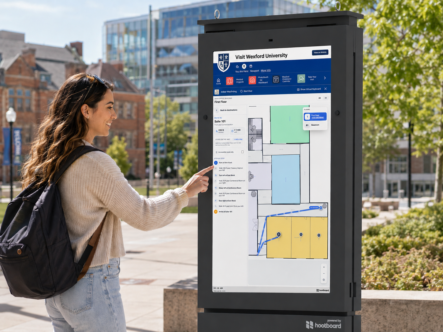 A student taps an outdoor HootBoard kiosk on a university campus, following step-by-step campus wayfinding directions to a room.